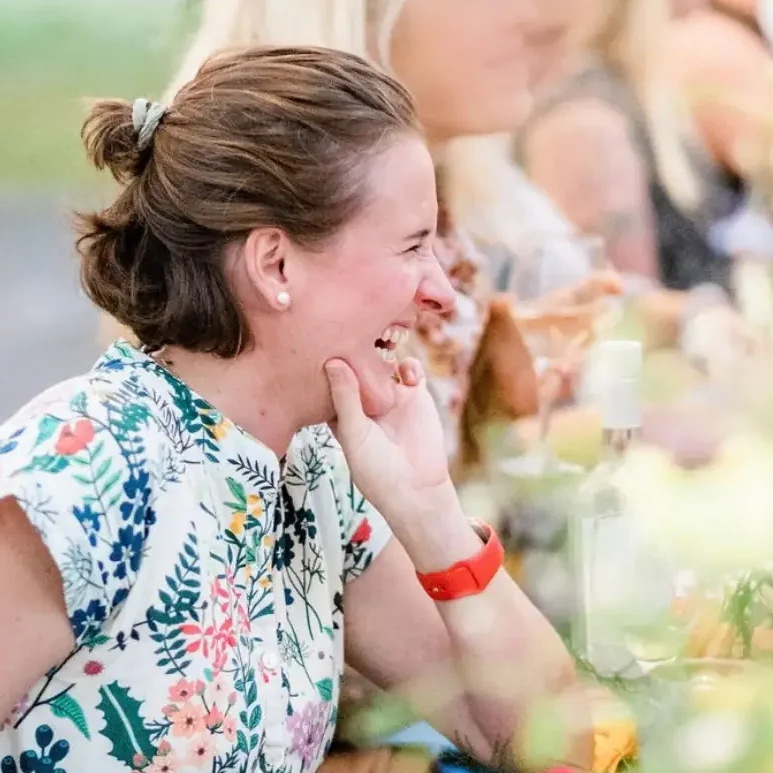 Alba laughing with guests at a long table set with flowers